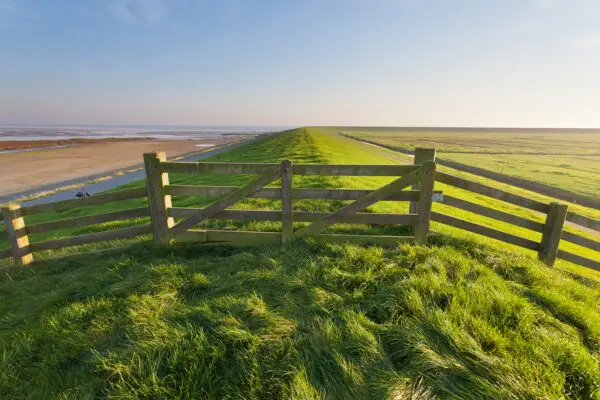 Een hek op een dijk met grasbekleding.