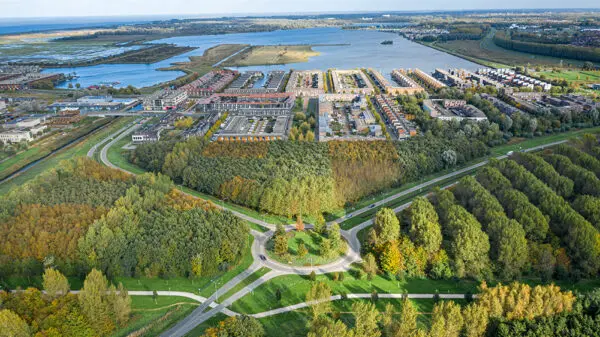 Een luchtfoto waarop water, groen en een woonwijk te zien is.