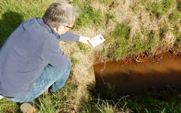 Een man is aan het meten in een bruine sloot.