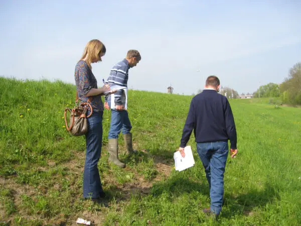 Drie personen lopen op een dijk en maken aantekeningen.
