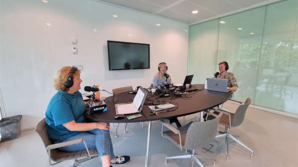 3 mensen in een vergaderruimte met podcast microfoons